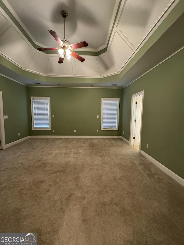 empty room featuring a tray ceiling, ceiling fan, carpet floors, and ornamental molding