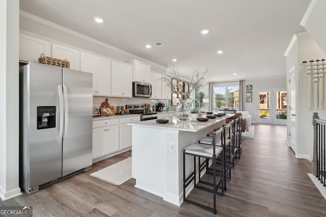 kitchen featuring wood-type flooring, appliances with stainless steel finishes, white cabinetry, a breakfast bar, and a center island with sink