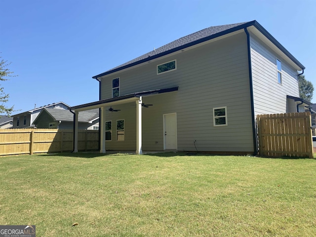 rear view of house with a ceiling fan, a lawn, and fence