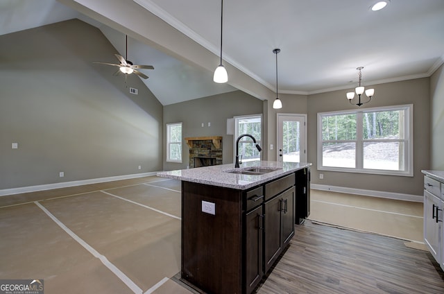 kitchen featuring ceiling fan with notable chandelier, an island with sink, sink, a stone fireplace, and light hardwood / wood-style floors