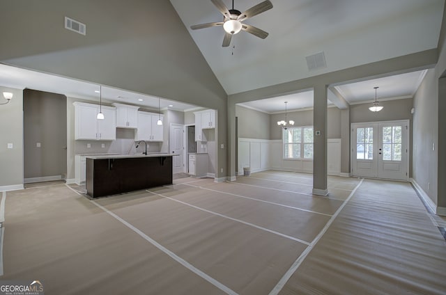 unfurnished living room with high vaulted ceiling, ceiling fan with notable chandelier, crown molding, and french doors