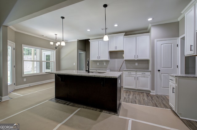 kitchen with white cabinets, light hardwood / wood-style flooring, light stone counters, a notable chandelier, and an island with sink