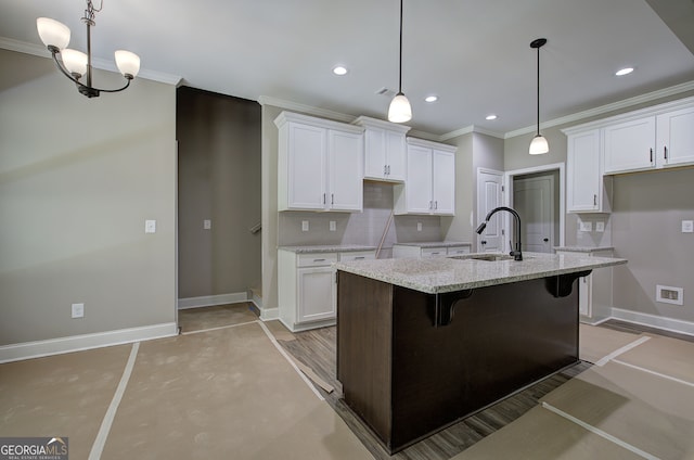 kitchen with decorative light fixtures, light stone countertops, white cabinetry, sink, and an island with sink