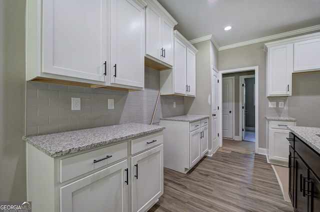 kitchen featuring white cabinets, light hardwood / wood-style flooring, light stone countertops, tasteful backsplash, and ornamental molding