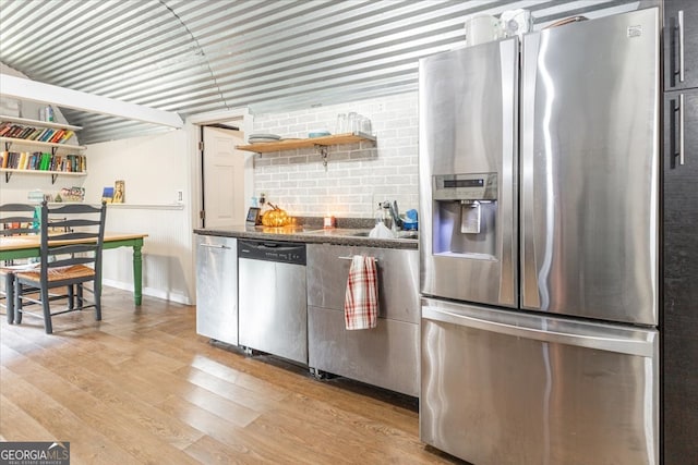 kitchen with stainless steel appliances, dark stone countertops, and light wood-type flooring