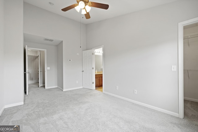 unfurnished bedroom with light colored carpet, a spacious closet, a closet, and ceiling fan