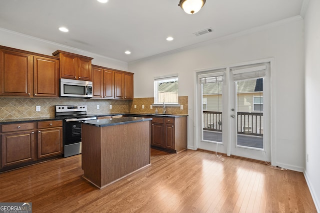 kitchen with appliances with stainless steel finishes, a kitchen island, crown molding, and hardwood / wood-style floors