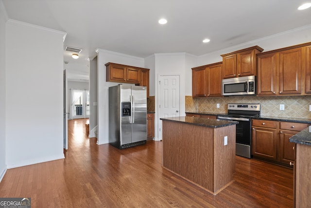 kitchen with backsplash, ornamental molding, stainless steel appliances, dark stone countertops, and a center island