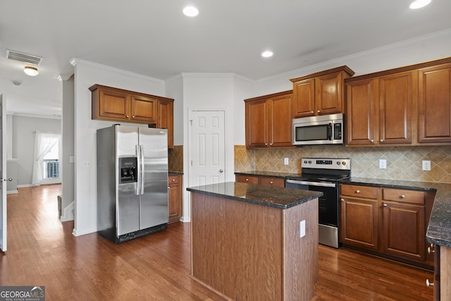 kitchen with appliances with stainless steel finishes, a center island, dark stone counters, and ornamental molding