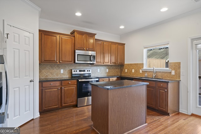 kitchen with dark wood-type flooring, crown molding, sink, a kitchen island, and stainless steel appliances