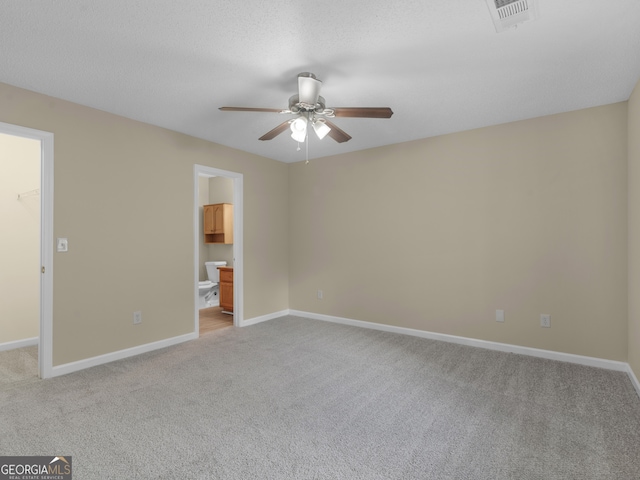 unfurnished bedroom featuring a walk in closet, a closet, ensuite bath, light colored carpet, and ceiling fan