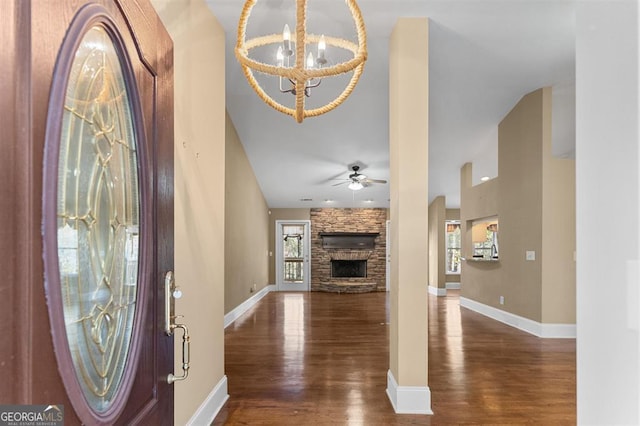 foyer entrance with ceiling fan with notable chandelier, a fireplace, and dark wood-type flooring