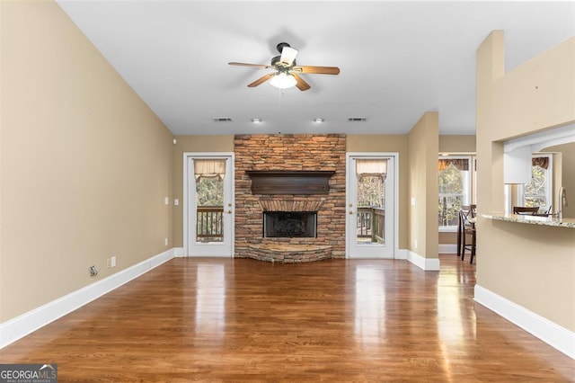 unfurnished living room with hardwood / wood-style flooring, ceiling fan, and a stone fireplace