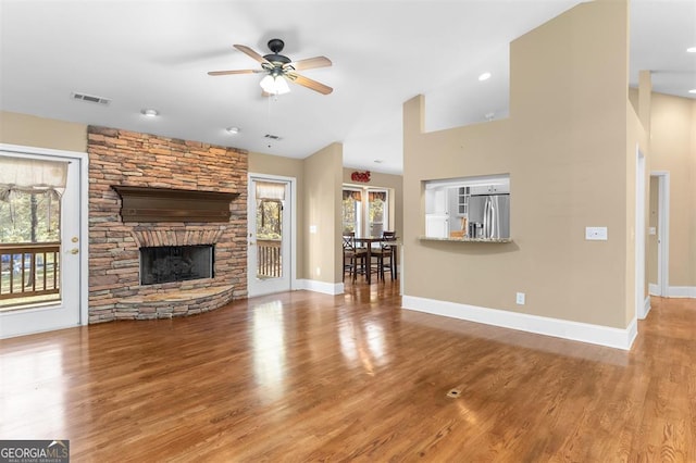 unfurnished living room featuring light wood-type flooring, a stone fireplace, plenty of natural light, and ceiling fan