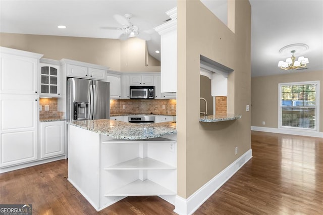 kitchen with kitchen peninsula, appliances with stainless steel finishes, ceiling fan with notable chandelier, white cabinetry, and lofted ceiling