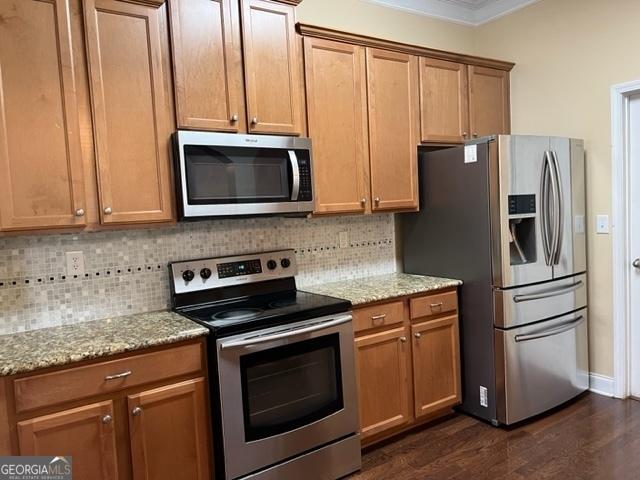 kitchen with dark wood-type flooring, light stone countertops, appliances with stainless steel finishes, and tasteful backsplash