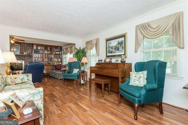 living area with hardwood / wood-style floors, ornamental molding, a textured ceiling, a brick fireplace, and ceiling fan