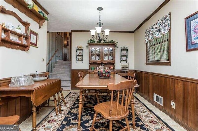 tiled dining room with ornamental molding, a chandelier, and wood walls