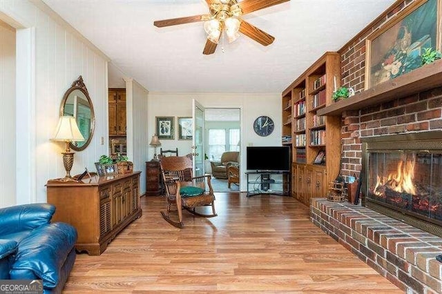 living room featuring built in shelves, ceiling fan, a brick fireplace, and light hardwood / wood-style floors