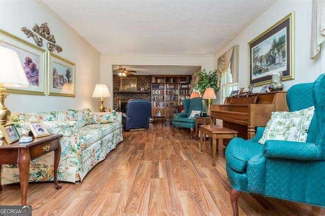 living room featuring a textured ceiling, wood-type flooring, ornamental molding, a brick fireplace, and ceiling fan