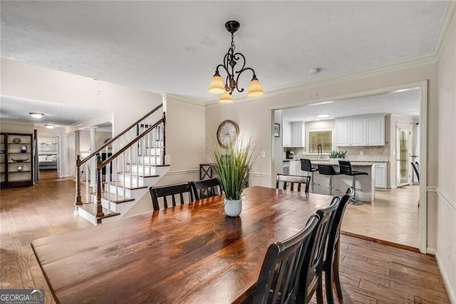 dining room with baseboards, stairs, light wood-style floors, ornamental molding, and an inviting chandelier