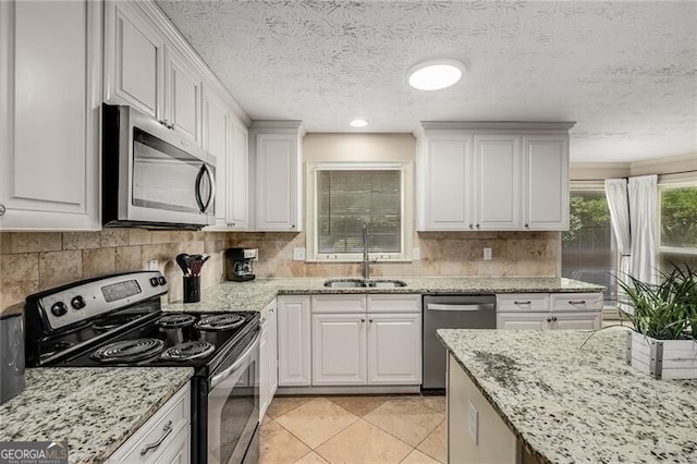 kitchen with stainless steel appliances, a sink, white cabinetry, decorative backsplash, and light stone countertops