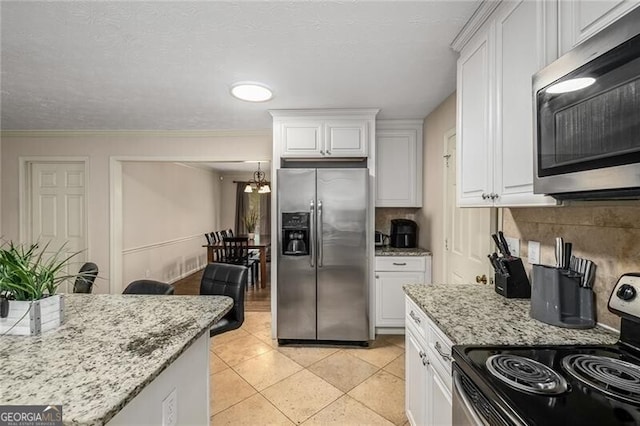 kitchen with white cabinets, decorative backsplash, appliances with stainless steel finishes, light stone countertops, and a notable chandelier