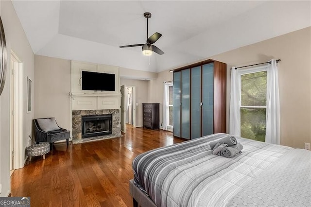 bedroom featuring ceiling fan, a raised ceiling, a fireplace, and wood finished floors