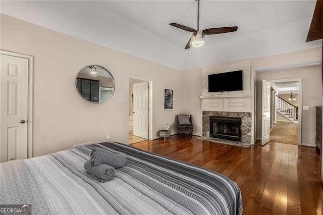 bedroom with a fireplace with flush hearth, ceiling fan, baseboards, and wood finished floors