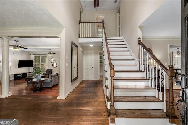 staircase featuring wood finished floors, a ceiling fan, baseboards, attic access, and decorative columns