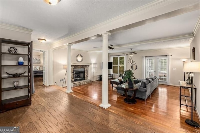 living area featuring decorative columns, hardwood / wood-style flooring, ceiling fan, ornamental molding, and a fireplace