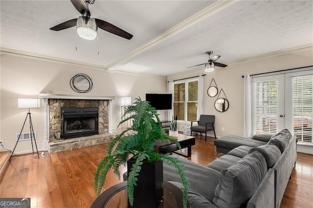 living area featuring french doors, ornamental molding, ceiling fan, a stone fireplace, and wood finished floors