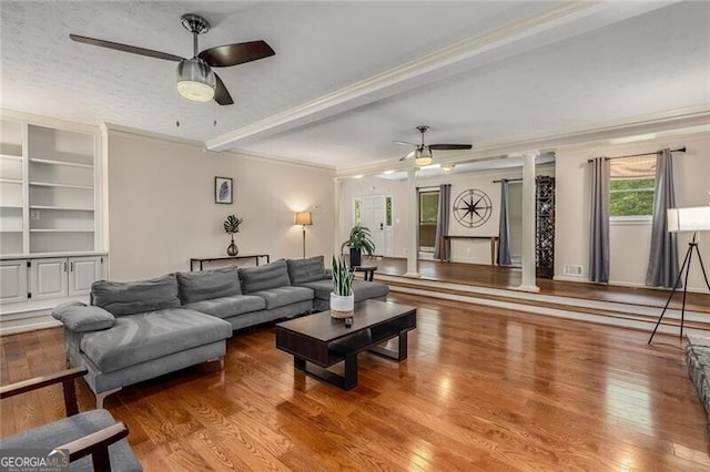 living room with beam ceiling, decorative columns, a ceiling fan, ornamental molding, and wood finished floors