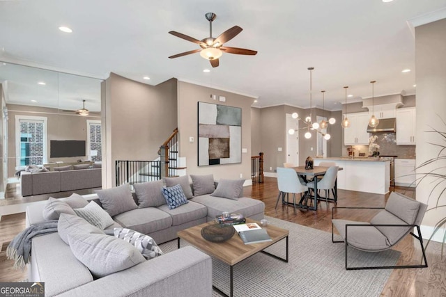 living room featuring light wood-type flooring, ceiling fan with notable chandelier, and crown molding