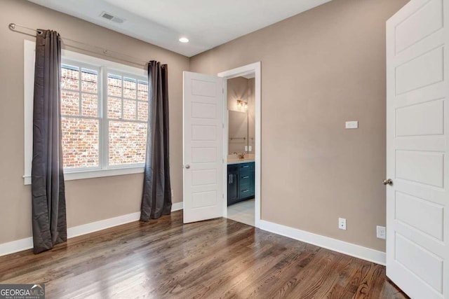 unfurnished bedroom with multiple windows, ensuite bath, and dark hardwood / wood-style floors