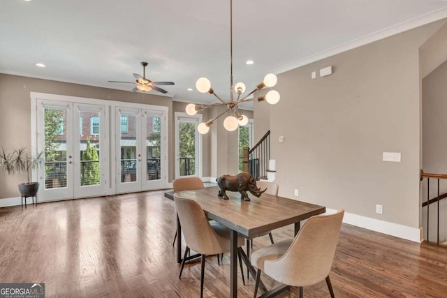 dining space with ceiling fan with notable chandelier, ornamental molding, dark wood-type flooring, and french doors