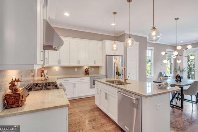 kitchen with appliances with stainless steel finishes, hanging light fixtures, light wood-type flooring, ventilation hood, and a center island with sink