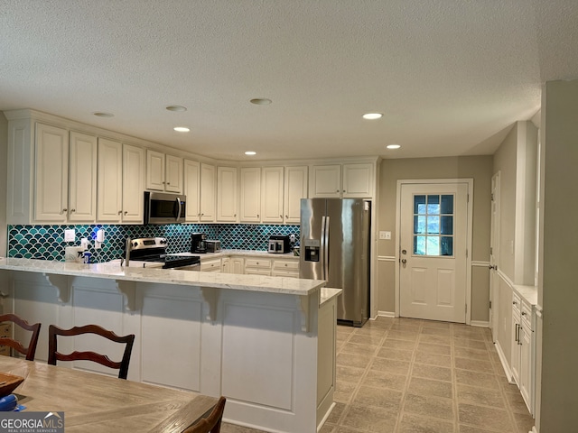 kitchen with stainless steel appliances, a kitchen bar, kitchen peninsula, and tasteful backsplash