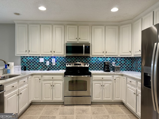 kitchen with light stone counters, appliances with stainless steel finishes, sink, and white cabinets