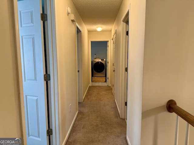 hallway featuring washer / dryer, a textured ceiling, and light carpet