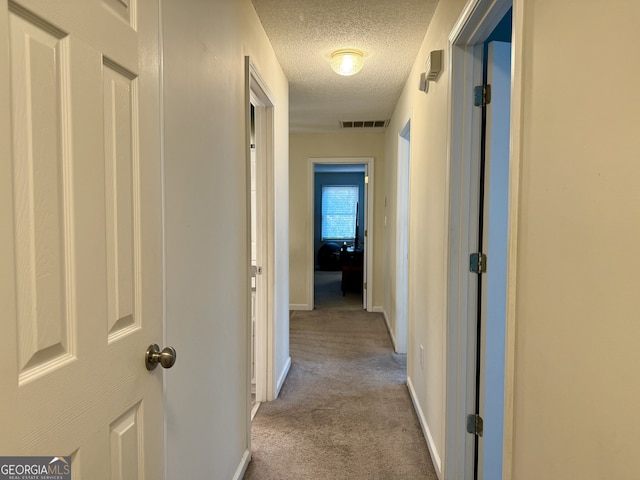 hallway with light carpet and a textured ceiling