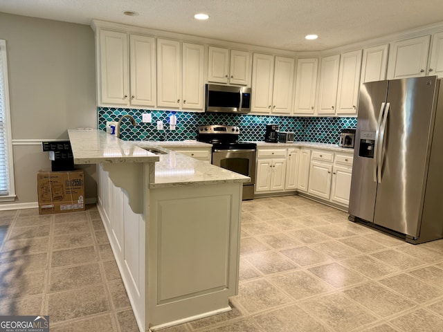 kitchen with kitchen peninsula, white cabinets, appliances with stainless steel finishes, a breakfast bar, and light stone counters