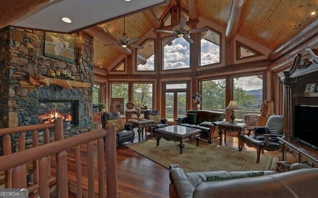 living room with ceiling fan, beam ceiling, high vaulted ceiling, hardwood / wood-style floors, and a stone fireplace