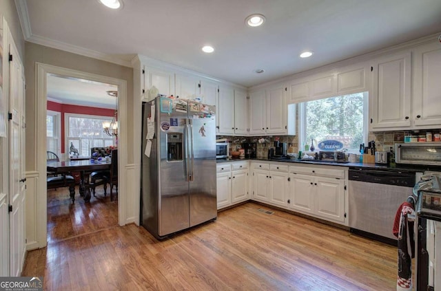 kitchen with appliances with stainless steel finishes, white cabinetry, light hardwood / wood-style flooring, and decorative backsplash