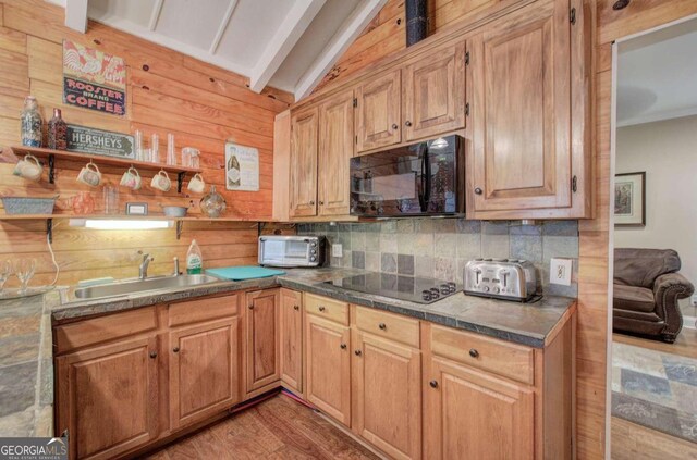 kitchen with hardwood / wood-style floors, wooden walls, black appliances, sink, and lofted ceiling with beams