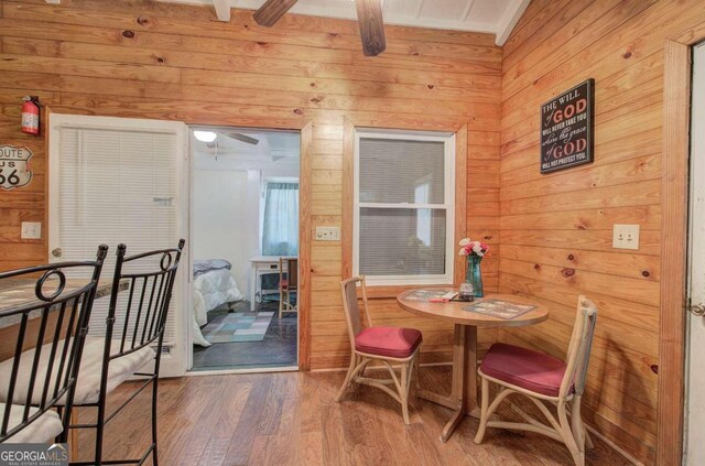 dining space with ceiling fan, wood walls, wood-type flooring, and lofted ceiling with beams