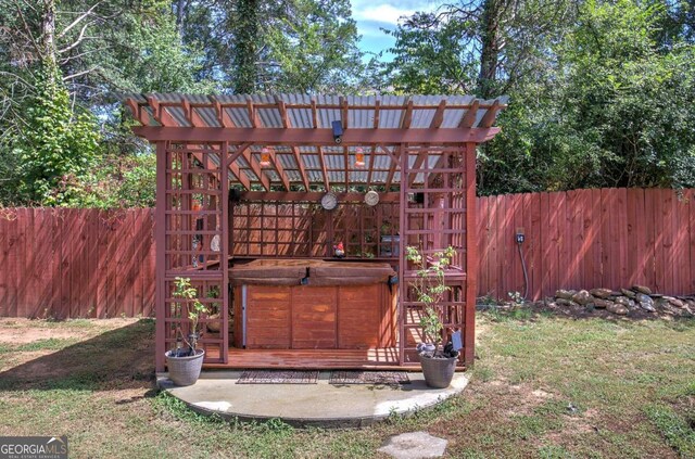 view of outdoor structure featuring a yard, a hot tub, and a pergola