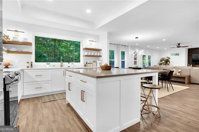 kitchen with stainless steel range with electric cooktop, a center island, ceiling fan, and light hardwood / wood-style floors