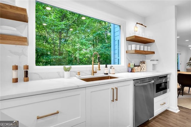 kitchen featuring stainless steel appliances, wood-type flooring, sink, light stone countertops, and white cabinets