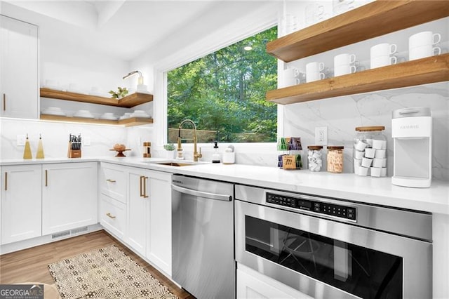 kitchen with light hardwood / wood-style floors, white cabinetry, sink, decorative backsplash, and stainless steel dishwasher